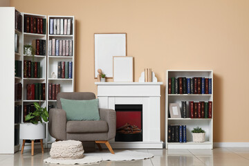 Obraz premium Cozy living room interior with fireplace, armchair, bookshelves, and blank picture frames on a beige wall