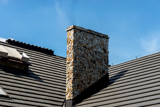 Stone covered chimney with slate roof under blue sky