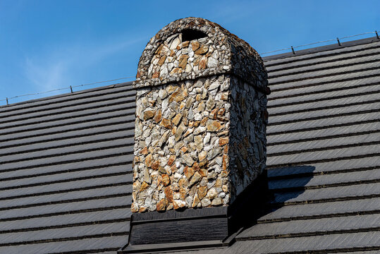 Stone chimney on traditional slate roof against blue sky