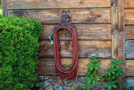 Red watering hose hanging on wooden house wall