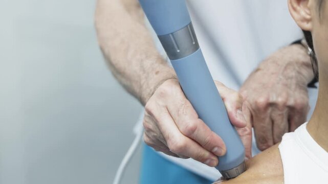 Medical specialist performing shockwave therapy on woman in contemporary clinical environment. Concept physical rehabilitation, pain therapy and healthcare technology.

