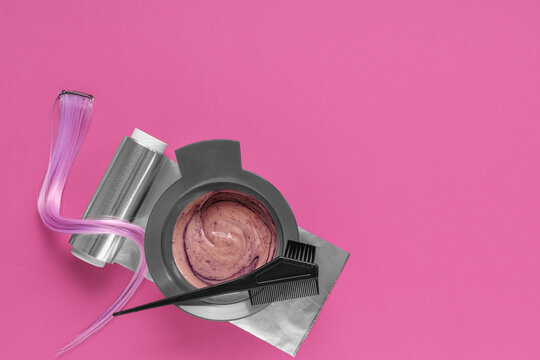 Hair dyeing tools with pink hair extension, color mixing bowl, brush, and aluminum foil on bright pink background
