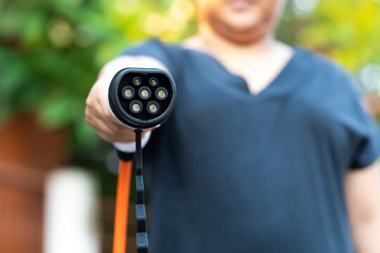 Close up electric car plug on woman hand for recharge plug in hybrid car at home or charging station. World Environment Day. save world save life concept.