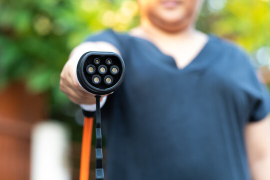 Close up electric car plug on woman hand for recharge plug in hybrid car at home or charging station. World Environment Day. save world save life concept.