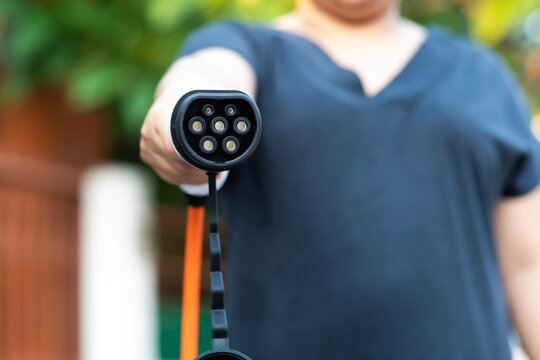 Close up electric car plug on woman hand for recharge plug in hybrid car at home or charging station. World Environment Day. save world save life concept.
