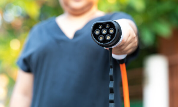 Close up electric car plug on woman hand for recharge plug in hybrid car at home or charging station. World Environment Day. save world save life concept.