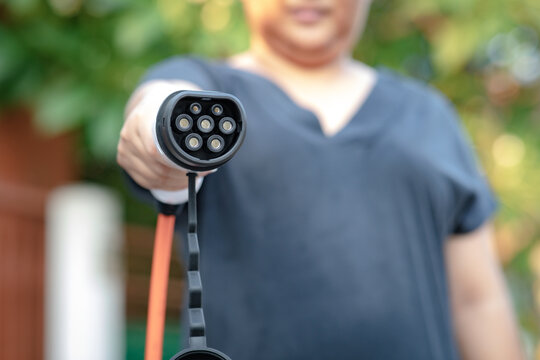 Close up electric car plug on woman hand for recharge plug in hybrid car at home or charging station. World Environment Day. save world save life concept.