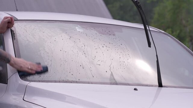 A man washes the car windows with a cloth before applying an anti-rain coating.