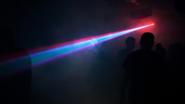 Dark underground club with single colorful laser beam through haze.