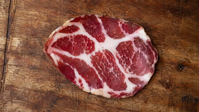 A slice of cured coppa on a wooden cutting board, top-down view.