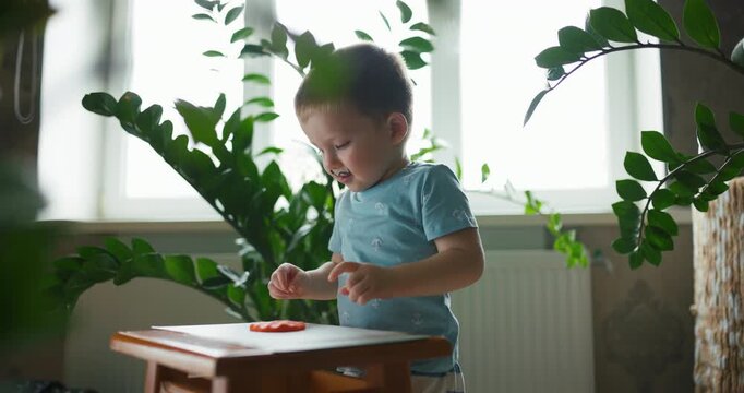 Funny little boy with painted mustache playing with orange modeling clay