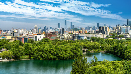 Obraz premium Urban Skyline with Green Park and Lake Under Clear Blue Sky