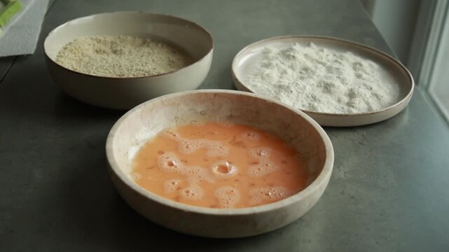 view of a three-bowl breading station arranged in a row with plain flour, whisked egg wash, and textured panko crumbs