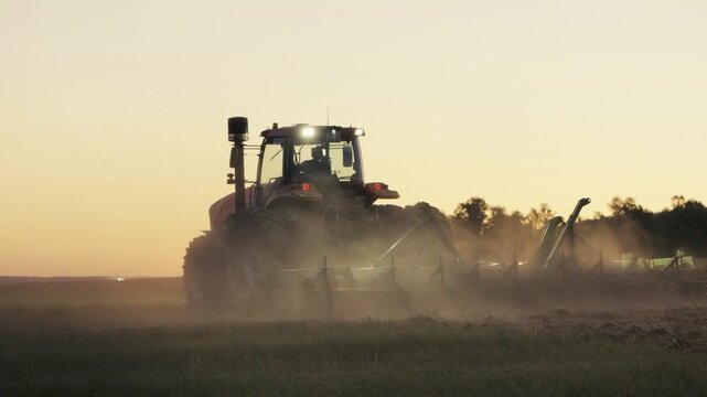 Modern Farm Tractor Preparing Soil At Sunset For Future Harvest And Food Production In Agricultural Field