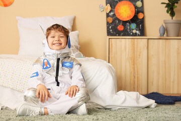 Happy young boy in astronaut costume sitting on floor, childhood dreams of space exploration and future career aspirations © Pixel-Shot