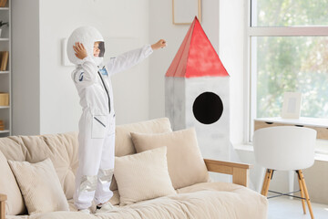 Young boy in astronaut costume standing on sofa, imagining space travel and future exploration © Pixel-Shot