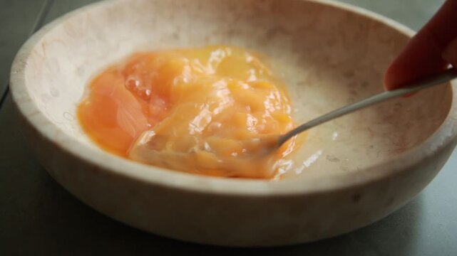 Close-up of a person's hand whisking raw eggs with a fork inside a ceramic bowl, beating the yolks and whites together
