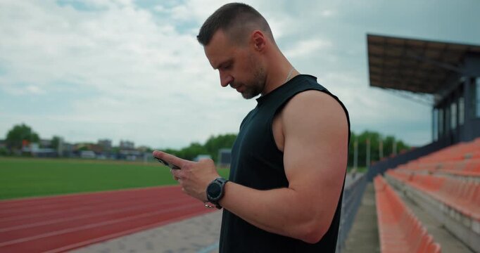 Professional runner looking at his smart watch on the stadium bleacher