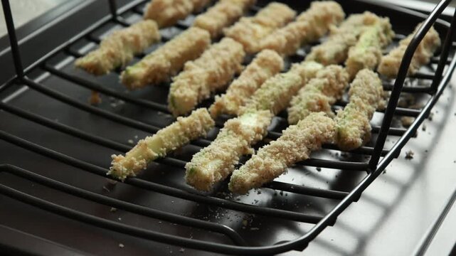 Close-up of raw zucchini fries coated in parmesan panko breadcrumbs and spices, neatly arranged on a wire rack ready for baking