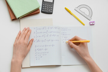 Naklejka premium Woman writing math formulas in copybook on light table