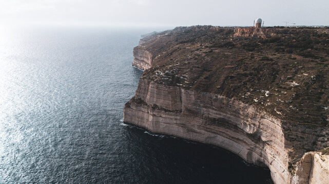 drone view of dingli cliffs chalky limestone coast on south malta island coast with Mediterranean Sea below at summer sunset golden haze above with green foliage on the land