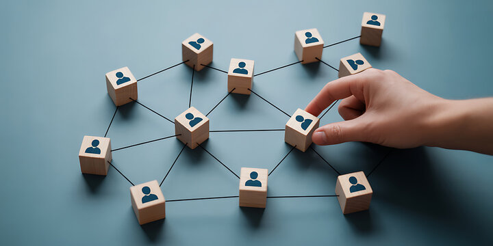 A hand placing a wooden block with a human icon into a network of connected blocks on a blue surface