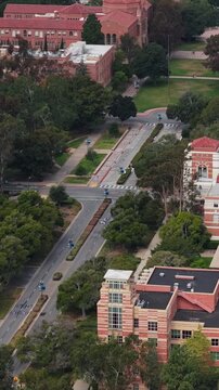 High angle establishing shot flying over University of California, Los Angeles campus buildings with traditional brick architecture and red tiled roofs in Southern California