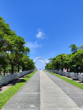 A barely discernible human figure walking across a massive bridge set amidst trees, with an archway in the background.