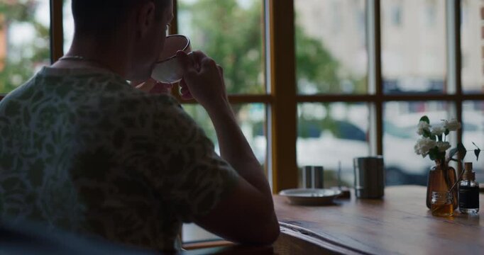 Cinematic back view of a man drinking tea and looking out of a cafe window