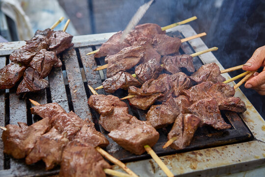 rows of succulent anticuchos sizzle and char under the practiced hands of a seasoned street vendor &mdash; the kind of aunty who has guarded her secret marinade recipe through generations