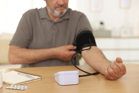 Man measuring blood pressure with sphygmomanometer at table indoors, closeup