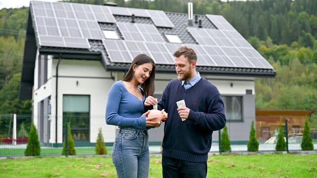 Couple managing finances and saving cash near residential home with solar roof. Video about energy efficiency, lower bills, responsible spending, and sustainable homeownership