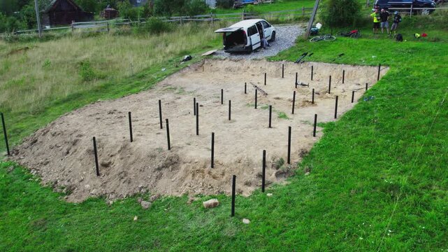 Pile foundation for future wooden frame house on mountain hillside. Drone view shows screw piles prepared for residential construction in scenic rural valley