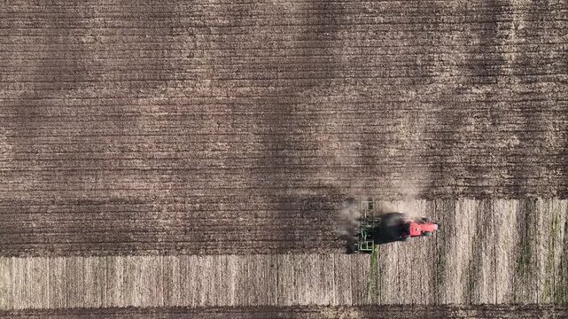 Agricultural tractor cultivating a field as drone flies parallel overhead, top view of soil cultivation, farm work, field prep and large farmland with copy space