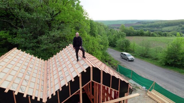 Builder on roof of wooden frame resort under construction. Drone view captures timber hotel complex with pool area on active woodland building site