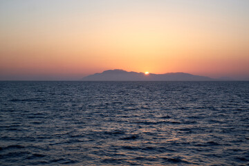 Obraz premium Peaceful serene sunset over the calm open sea with a mountainous island silhouette