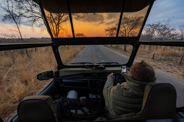 Fototapeta premium Safari vehicle driving at sunset on African bush road