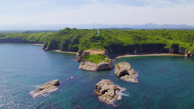 海上から加佐の岬と白い灯台を正面に捉えるドローン空撮 ホバリング・微後退 / Aerial drone hovering and slowly pulling back over the Sea of Japan facing Cape Kasa and lighthouse