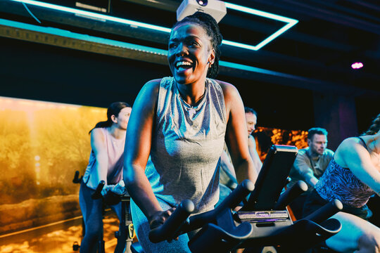 Smiling black woman leading intense indoor cycling workout in a diverse group fitness spin class