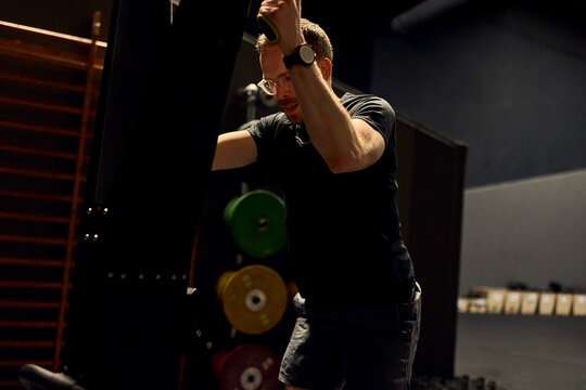 Focused man doing strength training on a cable machine in a dimly lit gym workout session