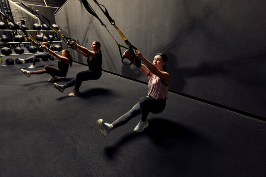 Women doing TRX suspension workout in a dark gym focusing on strength and balance