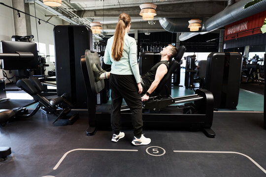 Personal trainer coaching man on leg press machine during strength training session in modern gym