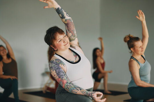 Body positive young woman with tattoos taking a yoga class with other female students and a teacher in a studio
