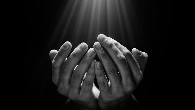 Cupped hands reaching upward toward a beam of light, black and white