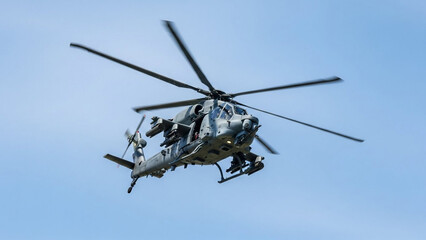 Fototapeta premium Modern combat helicopter in flight equipped with missiles and rockets under a clear blue sky during a military exercise.