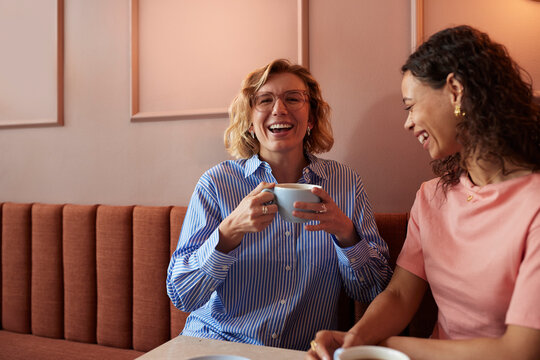 Two diverse friends share a coffee in a cozy cafe, smiling and enjoying a chat