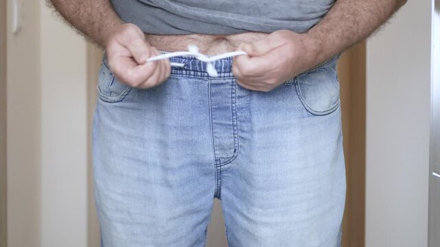 Overweight Man Trying to Put On Tight Jeans Closeup. Man with Big Belly Trying to Button Tight Jeans