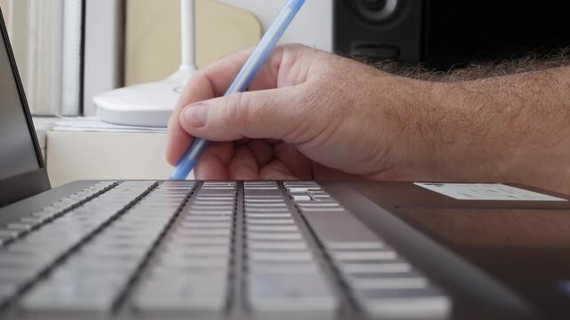 Hand Holding Blue Pen Writing on Laptop Keyboard