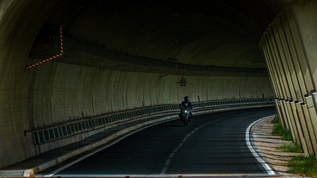  Ein einsamer Motorradfahrer f&auml;hrt durch eine Kurve in einem dunklen Betontunnel.