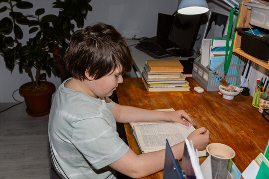 A schoolboy reading a book at a wooden table